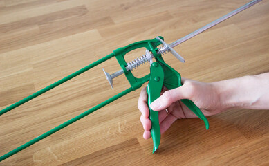 close up of a hand holding green metal caulking gun on wooden background