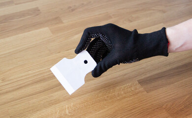 hand in a black glove holding a small white plastic (resin) scrapre isolated on wooden background