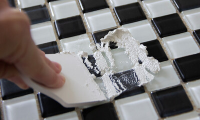 close up of hand spreading white grout on black and white tiles