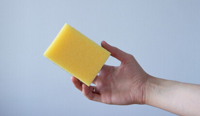 hand holding a yellow sponge on light-blue background