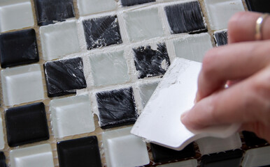 hand spreading grout on black and white small tiles