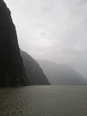 A dramatic and moody landscape of a calm fjord with steep, dark mountains disappearing into the...