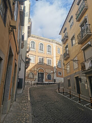 A picturesque steep cobblestone street winding through the historic old town of Lisbon, flanked by traditional European buildings
