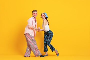Happy couple in retro outfits dancing on orange background, space for text