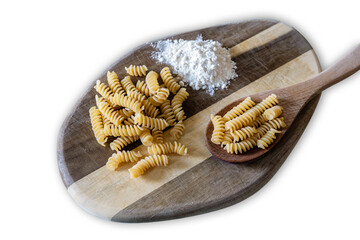 Composition of fusilli with flour and kitchen utensils on a wooden cutting board