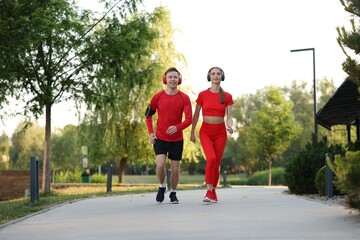 Happy couple in headphones running outdoors, low angle view. Morning exercise
