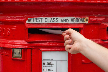 Male hand posting letter into red british post box on street, concept of communication, tradition, postal service