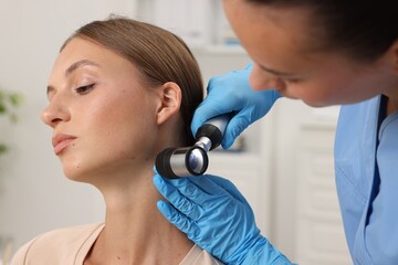 Doctor examining young woman's mole with dermatoscope in hospital