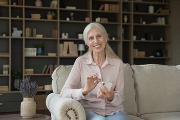 Modern tech on retirement. Home portrait smiling retired lady relax on couch in living room look at...