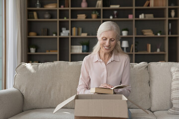 Book lover. Happy older woman online bookstore client open postal parcel with ordered items hold favorite paper edition volume satisfied with quick delivery high quality of printed literature received
