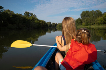 Mother and daughter paddling a canoe on a river surrounded by green trees
