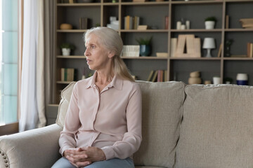 Ache of getting older. Sad depressed elderly grandmother pensioner sit alone on sofa at empty...