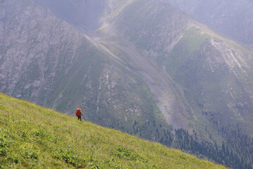A hiker with a backpack is walking down a slope with a view of a mountain peak. Trekking and...