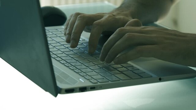 Dark cinematic close-up of hands typing on a laptop with moody lighting