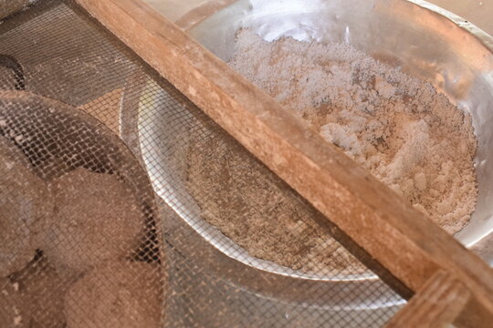 Receita tradicional nordestina de tapioca raiz, goma de mandioca misturada com coco ralado e sal no interior de bacia met&aacute;lica ao lado de peneira de ferro