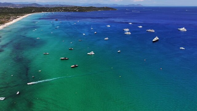 180&deg; right pan from north part of Pampelonne Beach across the bay with many expensive luxury yachts anchored, to south part beach, green wooded hilly landscape in background - 4k video aerial footage 
