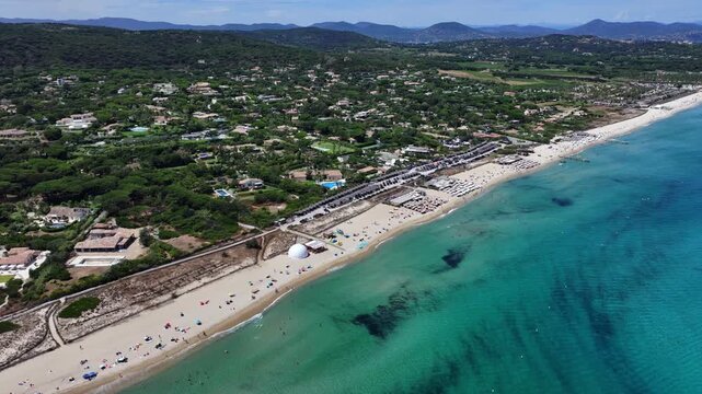 4k aerial video footage, flying backwards along Pampelonne Beach, located at coastline of Ramatuelle, C&ocirc;te d&rsquo;Azur, France, with people on the beach in water, green wooded hilly landscape in background