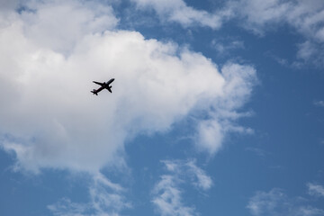 Airplane silhouette flying through blue sky with white fluffy clouds