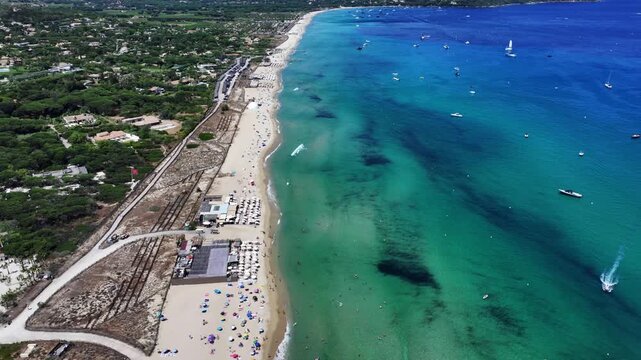 flying along famous Pampelonne Beach located at coastline of Ramatuelle, C&ocirc;te d&rsquo;Azur, France with people on the beach and in the water of Mediterranean Sea and many boats  - 4k aerial video footage