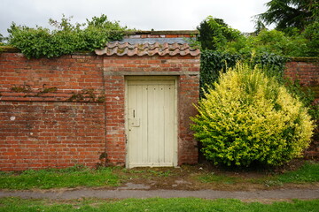 Scenic view of old brick garden wall with wooden door and lush spring foliage in the charming...