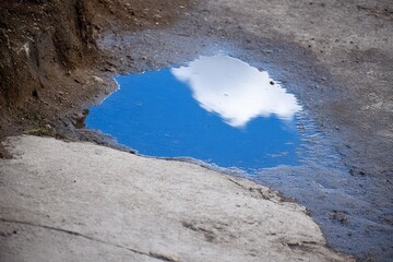 Puddle reflecting a blue sky with clouds on a gray concrete surface
