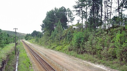 Obraz premium Scenic view of train tracks running through the lush, green rural landscape of Catas Altas, Minas Gerais. This railway, near the historic Bicame de Pedra, is a tranquil journey through nature.