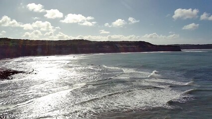 Aerial view of the stunning Praia de Pipa, also known as Pipa Beach, in Rio Grande do Norte, Brazil. The bright sun reflects on the ocean waves rolling towards the shore with cliffs behind.