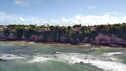 Stunning coastal landscape of Praia de Pipa in Rio Grande do Norte, featuring dramatic cliffs, lush vegetation, and the tranquil turquoise waters of the Atlantic Ocean on a beautiful sunny day.