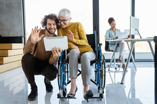 Business woman in wheelchair working with colleague in modern inclusive office. Diversity, support