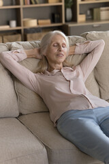 Enjoying daily rest. Happy lazy older lady lying on back on soft comfortable couch in living room...