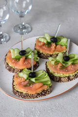 Sandwiches with salted salmon, black olives, avocado and cucumber on white plate