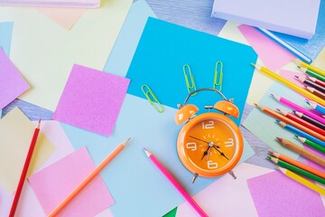 Back to school concept. Alarm clock, stationery and pastel colored paper on table, top view, flat lay.