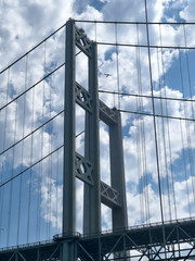 Columns and cables on the Narrows Bridge criss cross the sky just as a small plane flies by approaching the Narrows Airport.