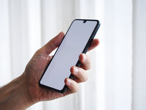 Hand Holding Black Smartphone with White Screen Showing Device Ready Text, Close Up Mobile Phone Mockup Against White Curtain Background.