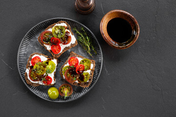 Italian bruschetta with ricotta, cherry tomatoes and balsamic sauce in a plate and black background top view copy space for text