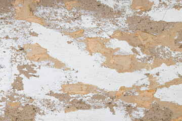 Old weathered wall surface with peeling white paint and exposed rough plaster texture. Rustic...