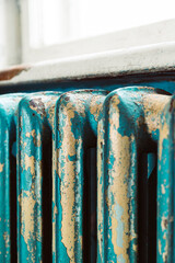 Close-up of an old cast iron radiator with peeling turquoise and beige paint. The rustic texture, cracked surface, and vintage industrial style create a distressed retro look, ideal for backgrounds