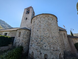 Historic Romanesque stone church with bell tower and apse under a clear blue sky in Noli, Italy,...