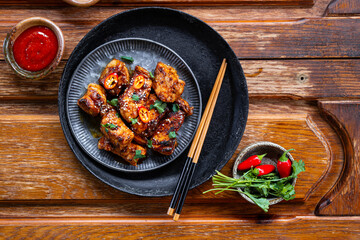 Asian roasted pork with sriracha sauce, hot pepper and sesame. Pieces of meat fried in soy sauce on wooden background top view copy space for text