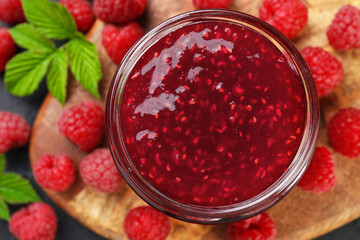 Sweet raspberry jam in glass jar and berries on table, top view