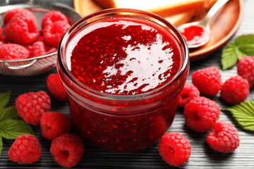 Sweet raspberry jam in glass jar and berries on dark gray wooden table, closeup