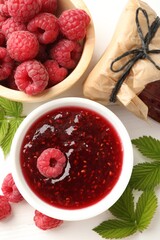 Sweet raspberry jam, berries and green leaves on white table, flat lay
