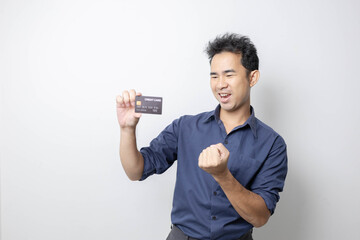 A man stands holding a cell phone, laptop, and credit cards. He is smiling happily and making...