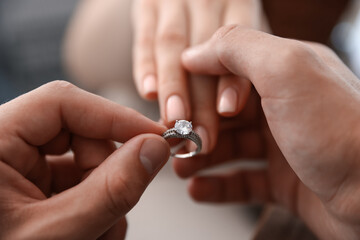 Making proposal. Man putting engagement ring on his girlfriend's finger indoors, closeup