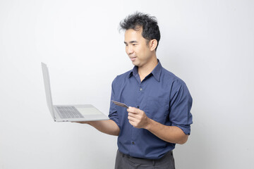 A man stands holding a cell phone, laptop, and credit cards. He is smiling happily and making...