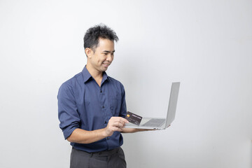 A man stands holding a cell phone, laptop, and credit cards. He is smiling happily and making various gestures for the camera.

