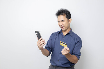 A man stands holding a cell phone, laptop, and credit cards. He is smiling happily and making...