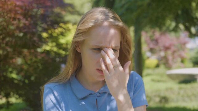 Woman suffering headache from magnetic storm weather sensitivity sunlight rubbing nose bridge feeling pain outdoors seasonal pressure fatigue emotional reaction physical discomfort.