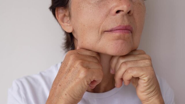Close-up of an older woman massaging her neck, showing visible signs of aging such as wrinkles and sagging skin. Self-care, mature beauty, natural aging process
