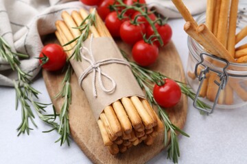 Delicious grissini sticks, rosemary and fresh tomatoes on light grey table, closeup